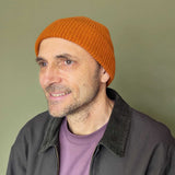 Man wearing an orange beanie and dark jacket against a green background