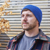 Man wearing a blue beanie and plaid jacket against a wooden background