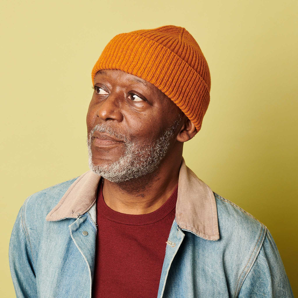 man in an orange catherine tough beanie against a green background