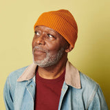man in an orange catherine tough beanie against a green background