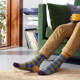 A man sitting on a sofa wearing socks featuring a green and blue diamond pattern