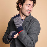A man wearing a dark gray wool coat models a pair of navy blue and gray striped fingerless knit gloves with a red accent stripe, set against a solid beige background.