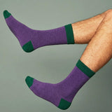 A [AIR OF PURPLE AND GREEN WOOL SOCKS WORN BY A MAN, WITH A GREEN BACKGROUND