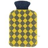 A knitted hot water bottle cover with a yellow and olive green argyle diamond pattern and a dark navy blue ribbed neck, shown on a plain white background.