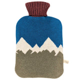 A knitted hot water bottle cover featuring a mountain design with a blue sky, white peaks, and a brown foreground, finished with a ribbed brown neck.