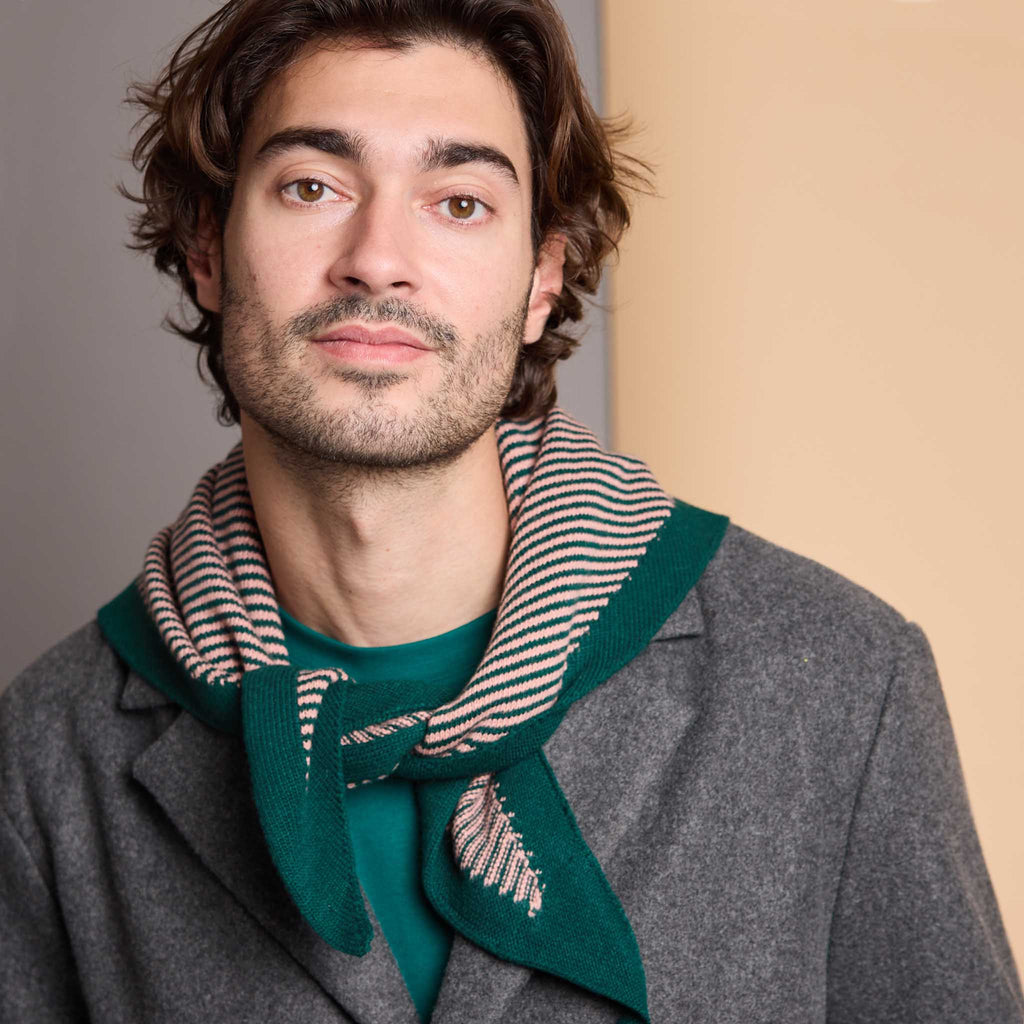 A man wearing a gray coat and green shirt, styled with a green and beige striped knit scarf.